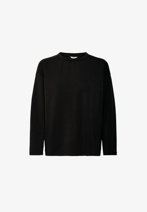 Melnā garas piedurknes krekls ar apaļu kaklu, izgatavots no gludas auduma. Iezīmējas ar nokritušām plecu daļām un brīvu piegriezumu. Nav redzamu rakstu vai akcentu.