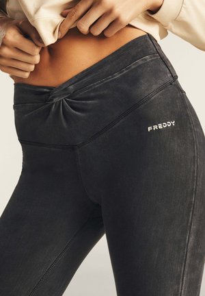 Leggings neri con dettagli annodati in vita, realizzati in un materiale liscio. Presentano il marchio "FREDDY" in argento sul lato.