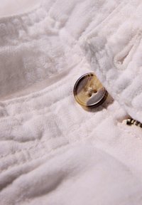 Witte stof met een quiltstructuur en een bruine knop. De knop heeft een gemarmerd patroon en is in de stof genaaid.