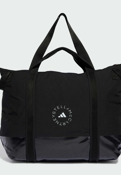 Sac de voyage noir en nylon avec un fond brillant, muni de doubles poignées, d'un logo circulaire et de sangles contrastantes. Design compact et fonctionnel.