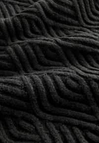 Tissu noir texturé avec un motif géométrique en zigzag. Fabriqué en matériau doux, il montre de la profondeur et de la chaleur à travers son tissage.