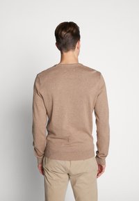 Maglione marrone lavorato a maglia con scollatura rotonda e maniche lunghe, presenta polsini e orlo a coste, realizzato in materiale morbido e testurizzato.