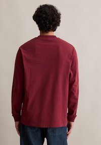 Langärmliges Hemd aus burgunderfarbigem Stoff mit einem runden Ausschnitt. Hat eine lockere Passform und gerippte Bündchen. Minimalistisches Design, keine sichtbaren Muster.