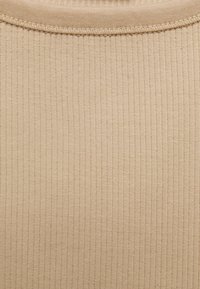 Gros plan sur un tissu en maille côtelée beige avec un col rond et un détail de couture visible au niveau du col.