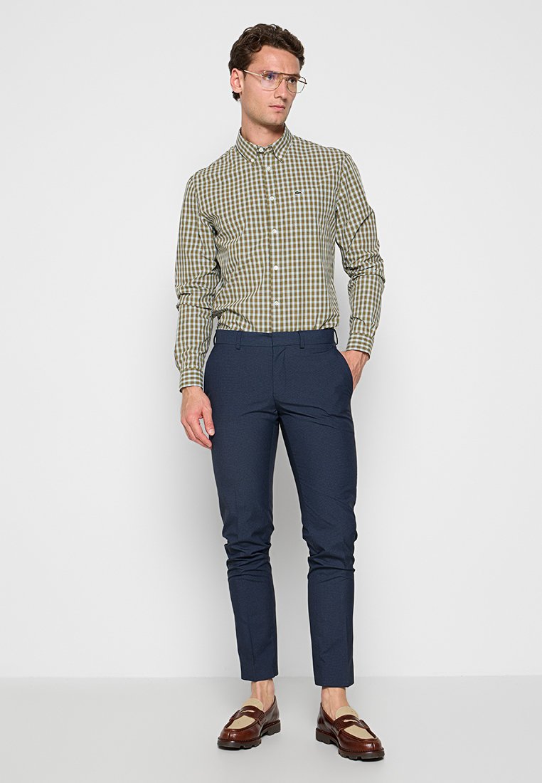 Grünes und beiges kariertes Hemd, lange Ärmel, Button-Down-Kragen; kombiniert mit dunkelblauen maßgeschneiderten Hosen und braunen Slippern.