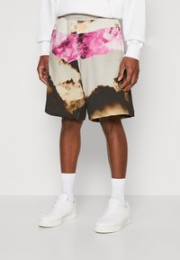 Shorts coloridos con un patrón texturizado en tonos marrones, beige y acentos en rosa brillante. La cinturilla es elástica y cuenta con costuras laterales.