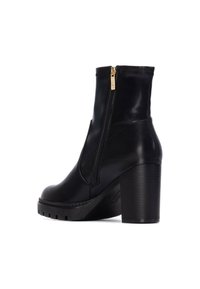 Botines de cuero negro con un alto tacón bloque, cremallera lateral y suela texturizada. Presentan acentos cosidos y un diseño elegante y ajustado.