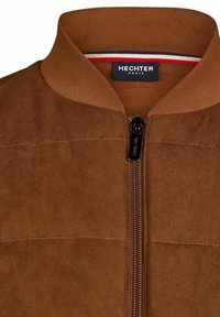 Braune Bomberjacke mit geripptem Kragen und Reißverschluss. Das Material wirkt weich und zeigt dezente Nähte sowie ein Etikett mit der Aufschrift "HECHTER PARIS".