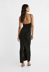 Schwarzes Kleid mit tailliertem Design und offenem Rücken. Verfügt über dünne Träger, geraffte Details und einen seitlichen Schlitz für Bewegungsfreiheit.