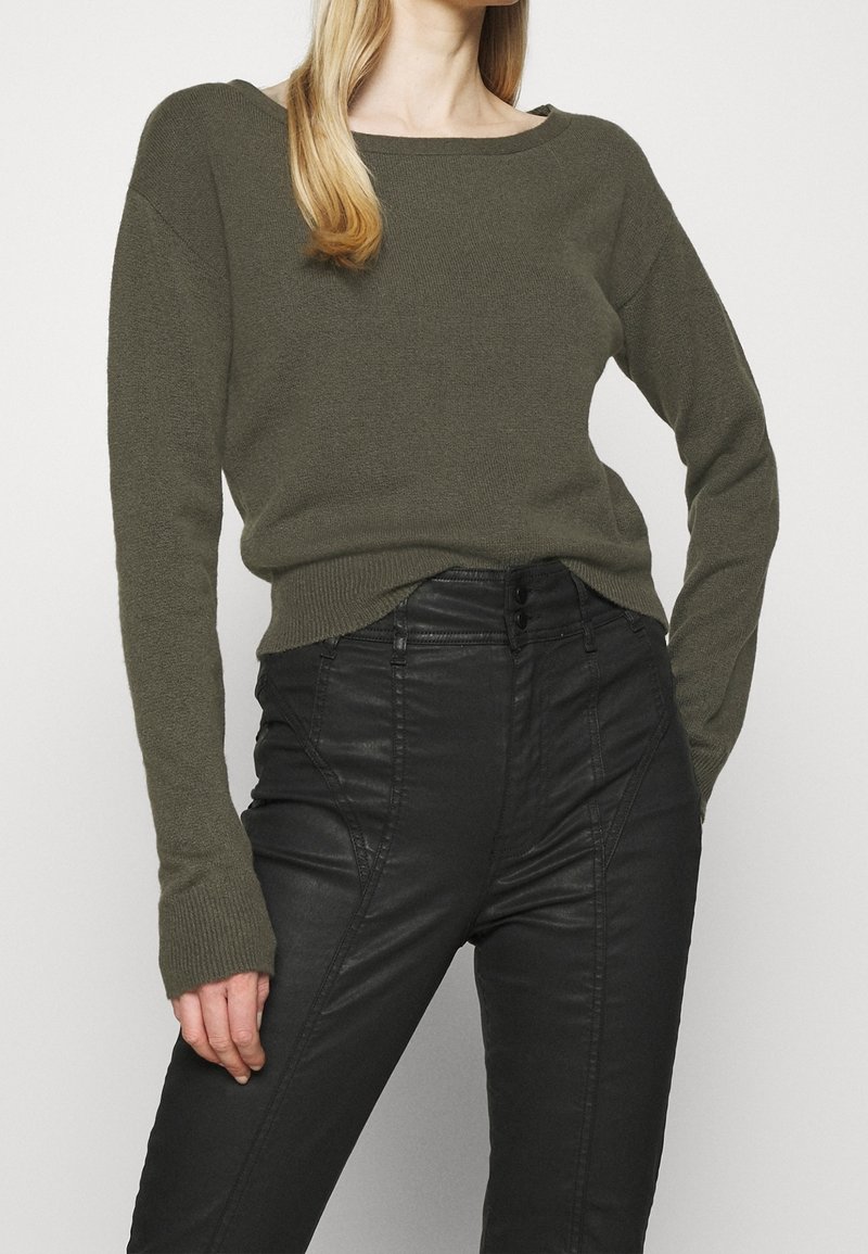 Pull en maille vert olive avec un col large et des manches longues, associé à un pantalon en cuir noir taille haute avec des coutures avant.