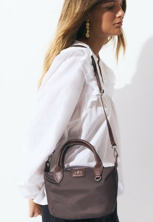 Sac à main en nylon marron avec des poignées en cuir texturé, comportant une bandoulière amovible et un petit patch logo à l'avant. Shape arrondie.