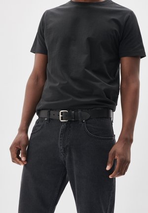Camiseta de algodón negra con escote redondo, combinada con jeans de mezclilla gris oscuro y un cinturón de cuero negro con hebilla plateada.