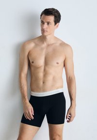 Zwarte boxershorts met een grijze Calvin Klein tailleband, gladde textuur, getailleerd ontwerp en een lengte tot halverwege de dij. Effen patroon zonder versieringen.