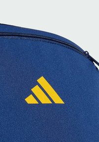 Marinblå sportväska med en gul tre-stripes-logotyp, slät yta och ett dragkedjestängning längs den övre kanten.