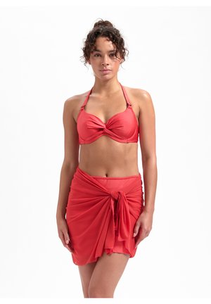 Set bikini rosso con top bandeau intrecciato e gonna avvolgente annodata in un tessuto leggero, che offre una texture liscia e un design aderente.