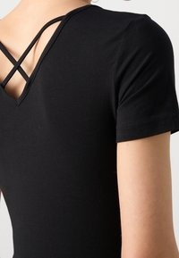 Svart bodysuit med V-formad rygg och korslagda remmar, korta ärmar och mjukt, elastiskt material för en åtsittande design.