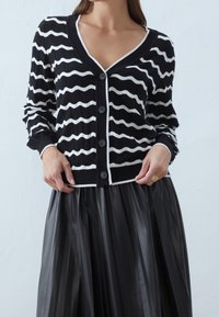 Randig svart och vit kofta med V-ringning, knäppning och kontrasterande vit kant. Mjuk stickad kvalitet med en avslappnad passform.