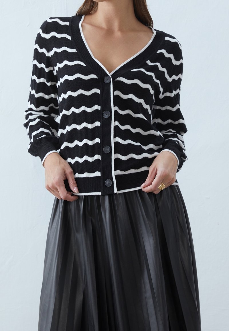 Randig svart och vit kofta med V-ringning, knäppning och kontrasterande vit kant. Mjuk stickad kvalitet med en avslappnad passform.