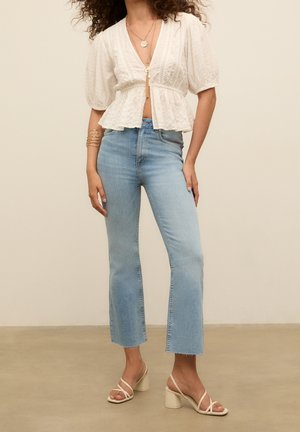 Hvid tekstureret peplum-top med korte ærmer, lys blå denim flared jeans og beige blokhælede sandaler. Guld smykkedetaljer.