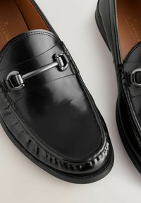 Sorte læder loafers med en glat finish, prydet med dekorativt sølvhardware og detaljeret syning langs kanterne.