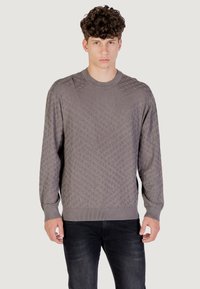 Pull en maille gris avec un motif en losanges, col rond, manches longues et poignets et ourlet côtelés. Porté avec un jean sombre.
