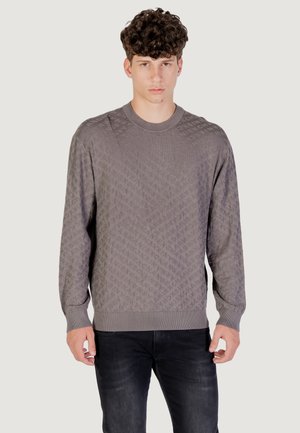 Maglione grigio lavorato a maglia con un motivo a rombi, scollo rotondo, maniche lunghe e polsini e orlo a coste. Indossato con jeans scuri.