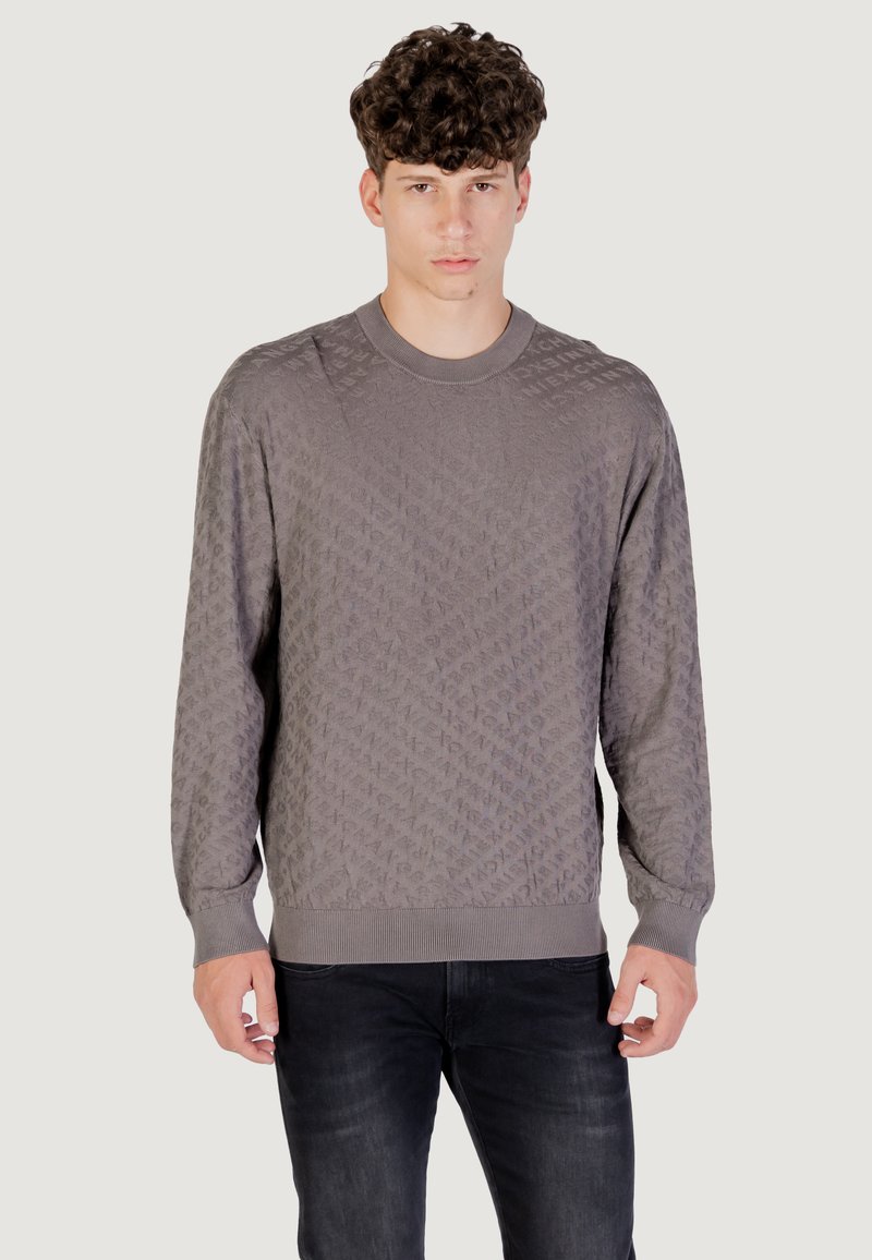 Pull en maille gris avec un motif en losanges, col rond, manches longues et poignets et ourlet côtelés. Porté avec un jean sombre.