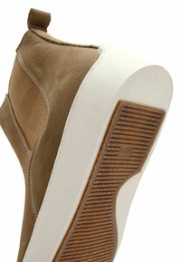 Sneaker in tela marrone con suola in gomma bianca, caratterizzato da una parte superiore testurizzata, cuciture a contrasto e un piccolo tallone per facilitare l'uso.