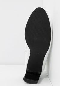 Weißer High Heel-Schuh mit einer glatten Textur-Oberfläche und einer schwarzen Gummisohle. Verfügt über einen schmalen Absatz und die Größe ist auf der Außensohle markiert.