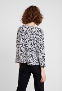 Graues Langarmshirt mit schwarzem Leopardenmuster. Hat eine lockere Passform und einen runden Ausschnitt, gefertigt aus einem weichen, strukturierten Stoff.