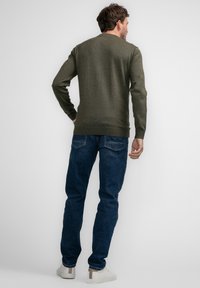 Olijf groene gebreide trui met een ronde hals, gecombineerd met blauwe spijkerbroeken en witte sneakers. Heeft een aansluitend ontwerp en geribde mouwen.