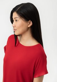 Röd kortärmad topp med rund halsringning och ett mjukt, lätt tyg. Ärmarna har subtila uppvikta manschetter.