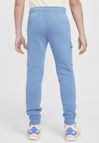 Modré tepláky se stahovací šňůrkou v pase, zúženými nohavicemi a dvěma postranními nákladními kapsami. Materiál vypadá měkce a má strukturovaný povrch.