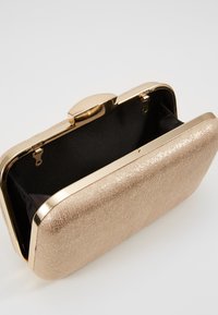 Clutch metálico en rosa dorado con superficie texturizada. Cuenta con un cierre en tono dorado y un interior de tela negra. Forma rectangular compacta.
