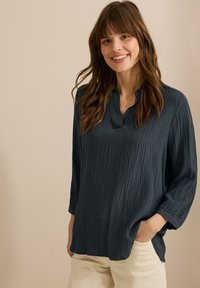 Mörkblå blus med textur, V-ringning och ärmar i 3/4 längd, med en lös passform och framträdande vertikala linjer.