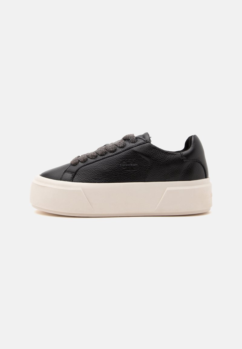 Μαύρο δερμάτινο sneaker χαμηλής κοπής με χοντρή λευκή πλατφόρμα και σκούρα γκρι κορδόνια, πλευρική όψη σε απλό φωτεινό φόντο.