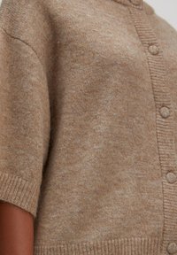 Beige gebreide cardigan met korte mouwen, knoopsluiting aan de voorkant en geribbelde onderrand. Zachte textuur en subtiele kleurvariaties door de stof.