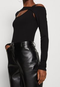 Body nero a coste con maniche lunghe, caratterizzato da un dettaglio cut-out sul collo e spalle scoperte. Abbinato a pantaloni in pelle nera a vita alta.
