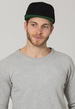 Cappello nero con visiera verde, indossato con una maglietta a maniche lunghe grigio chiaro con maniche raglan e dettagli di cucitura sottili.