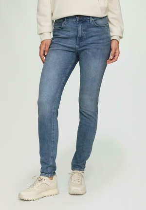 Jean bleu clair à coupe slim, avec un design classique à cinq poches, des passants de ceinture et un délavage subtil. Associés à des baskets beiges.
