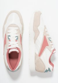 Sneakers bianchi in rete e scamosciato beige con dettagli rosa, caratterizzati da un design testurizzato e una suola in gomma bianca. I lacci sono bianchi.