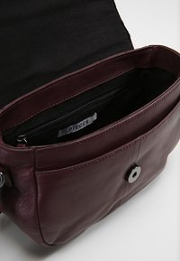 Bordeauxrode lederen handtas met een binnenvak met rits. Het interieur is voorzien van een zwarte stoffen voering en een magnetische druksluiting.