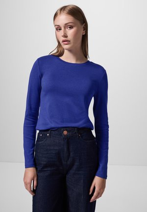 Chemise à manches longues d'un bleu vif, en tissu doux. Dotée d'un col rond, elle est associée à un pantalon en denim foncé taille haute.