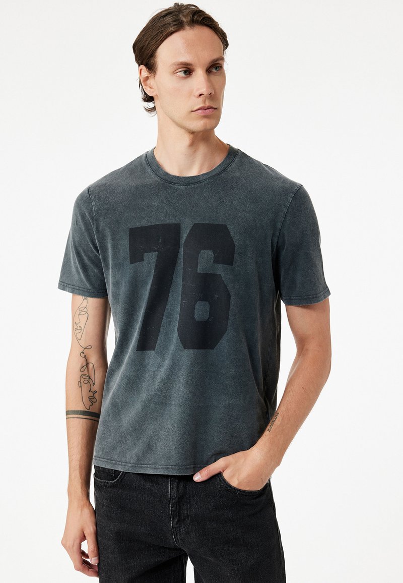 Czarny t-shirt wykonany z bawełny, z dużym czarnym nadrukiem '76' z przodu. Krótkie rękawy i okrągły dekolt.