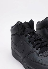 Sneakers neri alto in pelle texture, con dettagli cuciti, forature e lacci piatti neri con una suola leggermente rialzata.