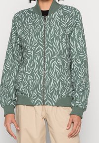 Bomber jacket in muted green with a leafy pattern, ribbed cuffs and hem, zip closure, and lightweight fabric texture.