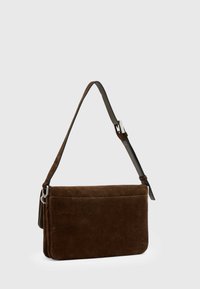 Brun suedet crossbody taske med flad design, justerbar læderrem, sølv hardware og en frontlomme til opbevaring.
