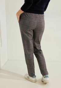 Szare spodnie w kratę z różowymi i zielonymi akcentami, slim fit, z tylnymi kieszeniami, w zestawieniu z białymi trampkami z niebieskim logo.