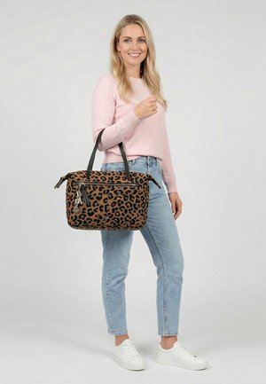 Femme portant un pull rose clair et un jean tenant un sac à main imprimé léopard marron avec des sangles noires et des détails zippés.