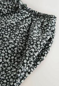 Tela con patrón floral en blanco y negro con cintura elástica fruncida, probablemente parte de una falda o pantalones.